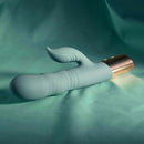 The Shimmy Vibrator with Clitoral Stimulator Green on soft textured fabric, showcasing its design and color.