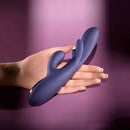 Bow Down Vibrator with Clitoral Stimulator Purple in a hand against a purple background.