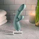 Evolved Rub Me Tender G-spot Clitoral Stimulator displayed on a stand with candles and towels in background.