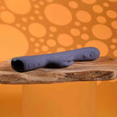 Poppin Good Time Rechargeable Rabbit Vibrator Purple resting on a wooden surface with a playful orange backdrop.