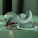 Spiral Charm Rechargeable Clitoral Stimulator Green on a reflective surface with decorative glass orbs.