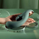 Spiral Charm Rechargeable Clitoral Stimulator Green resting on a hand beside decorative glass spheres.