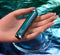 Hand holding Playboy Emerald glass tip vibrator with sleek design and diamond-pattern base on a shimmering surface.