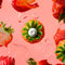 Fresh strawberries with a white F-shaped mint surrounded by juicy strawberry slices and droplets on a pink background.