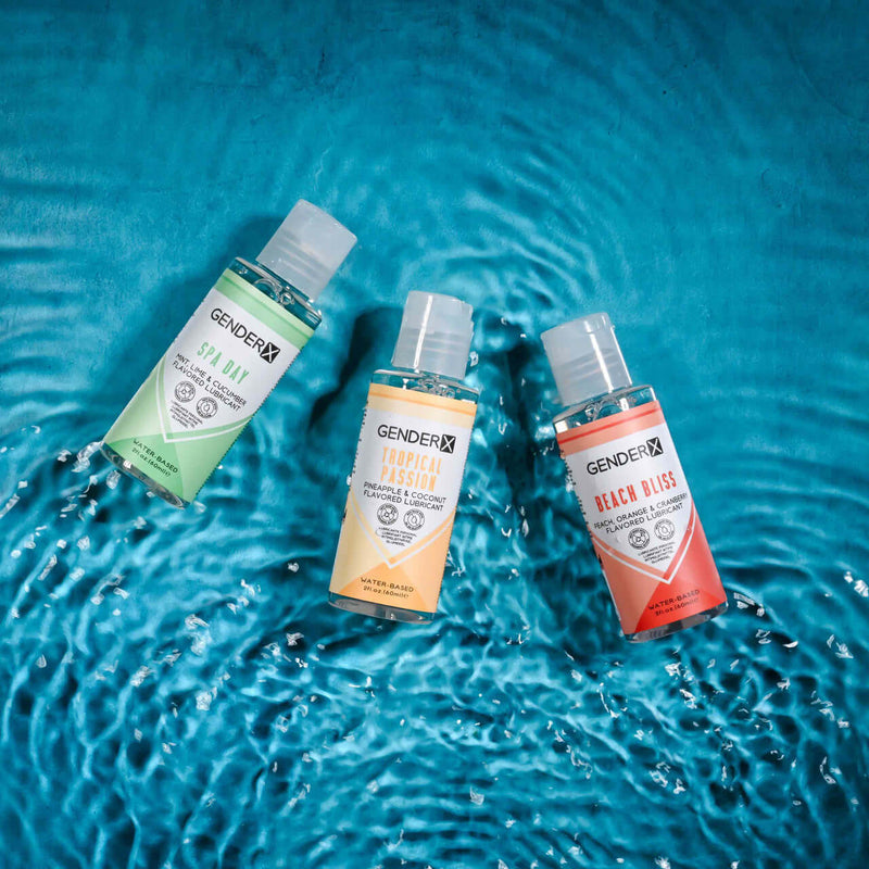 Gender X Flavored Lube Travel 3-Pack with Spa Day, Tropical Passion, and Beach Bliss bottles on water surface.