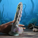 Gender X Monsters Ball Thrusting Vibrating Dildo with Remote Control held by a hand against an underwater background.