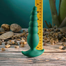 Gender X The Rattler Twirling Prostate Vibrator Green displayed with a ruler for size comparison on a wooden surface.