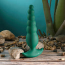 Gender X The Rattler Twirling Prostate Vibrator Green displayed on a textured stone surface with pebbles.