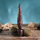 Gender X Into the Deep Silicone Vibrating Dildo Purple on rocks with seashells in ocean-inspired setting.
