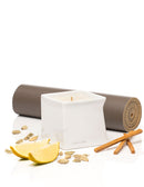 Jimmyjane Natural Massage Oil Candle 4.5 Oz Santal with lemon, cardamom, and cinnamon sticks on yoga mat.
