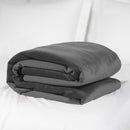 Liberator Fascinator Throw Grey folded on a bed, offering plush comfort and moisture protection for intimate adventures.
