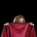 Woman holding Liberator Fascinator Mini Waterproof Throw Merlot against a black background.