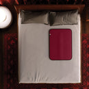Liberator Fascinator Mini Waterproof Throw Merlot on a bed, protecting sheets with an elegant design.