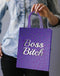 Person holding a purple Boss Bitch Gift Bag with elegant woven handle, perfect for VIP party gift wrapping.