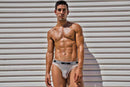 Male Power Peep Show Low Rise Thong White S M worn by a muscular man against a textured background.