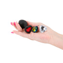 Glams Xchange Heart Silicone Anal Plug Small Black alongside colorful heart-shaped anal plugs in a hand.