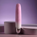 Pink rechargeable silicone vibrator with angled tip and gradient design against a soft purple background.