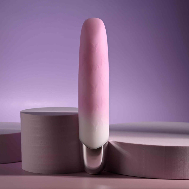 Pink rechargeable silicone vibrator with angled tip and gradient design against a soft purple background.