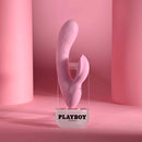 Playboy Rabbit Party Silicone Rabbit Vibrator Purple displayed on a clear pedestal with pink backdrop.