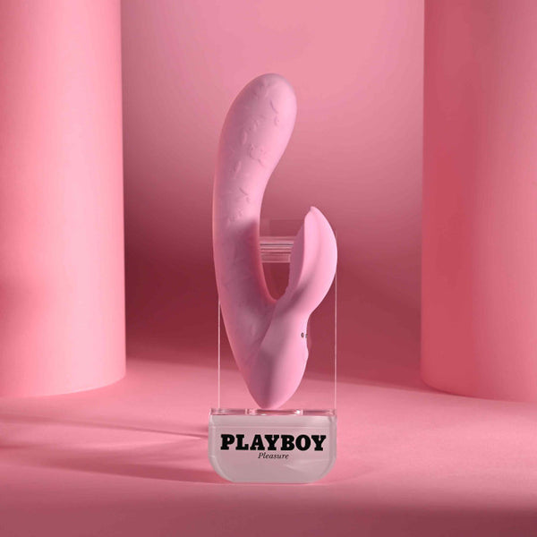 Playboy Rabbit Party Silicone Rabbit Vibrator Purple displayed on a clear pedestal with pink backdrop.