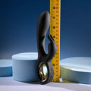 Black silicone dual vibrator with chrome ring, measuring ruler beside for size reference.