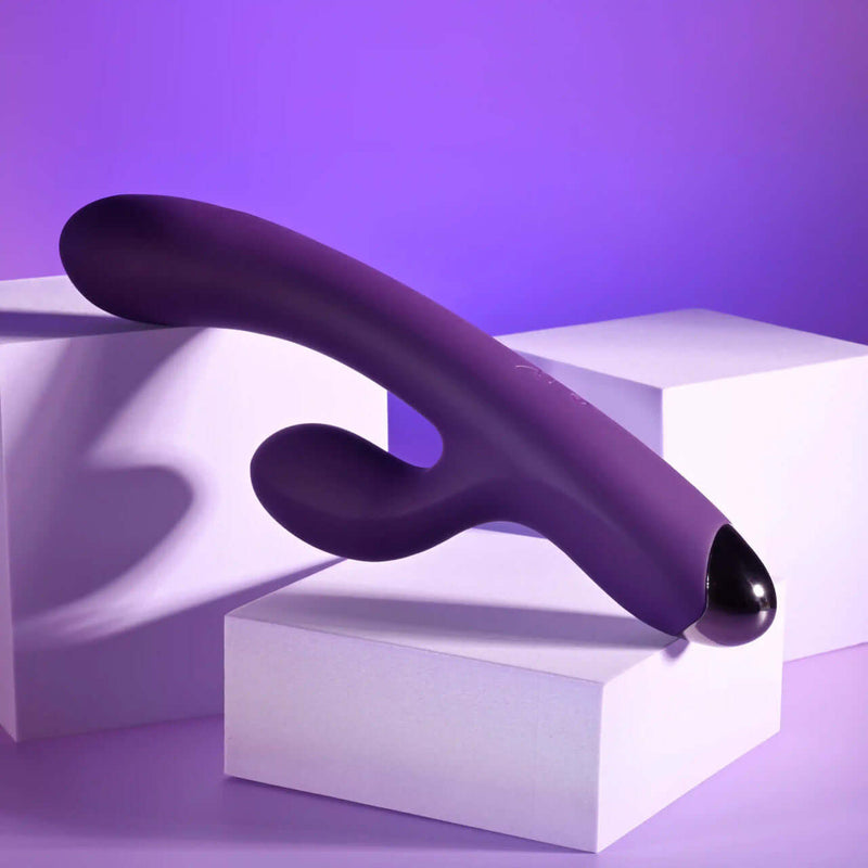 Playboy New Crush rechargeable silicone dual vibrator in purple against a soft purple backdrop.