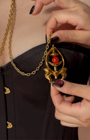Close-up of a hand holding gold Pulling Chain Nipple Clamps with red accent, showcasing intricate design and chain details.