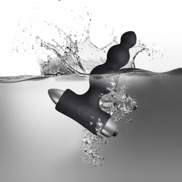Petite Sensations Bubbles Black silicone vibrating anal plug submerged in water, showcasing its sleek design and functionality.