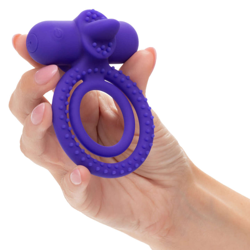 Purple silicone rechargeable vibrating couples enhancer with dual support held in hand.