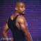 Man wearing Radiance Muscle Tank Top with rhinestone accents against a brick wall background.