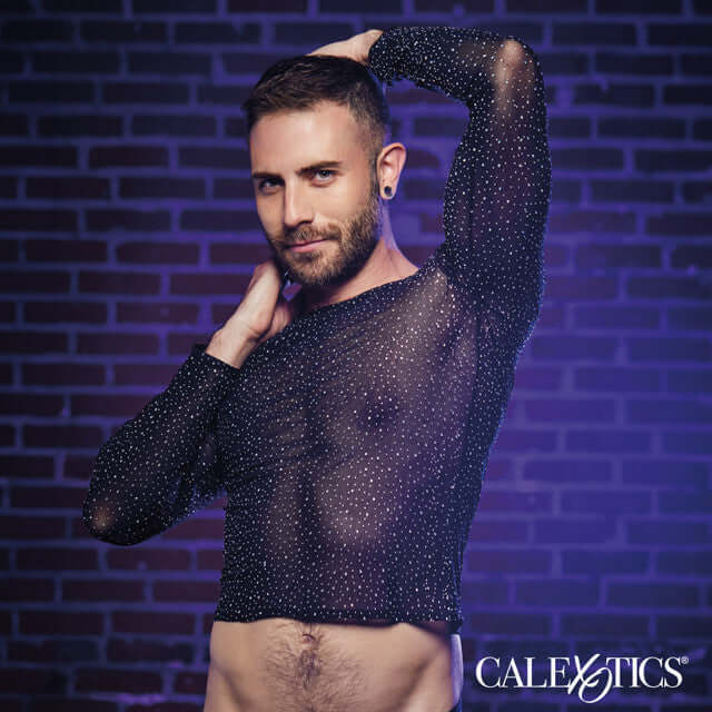 Person modeling dazzling mesh long sleeve shirt with rhinestone accents against brick wall.
