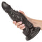 "Hand holding Monster Dong The Colossus 9.75” liquid silicone dildo with suction cup base, featuring detailed, life-like structure"