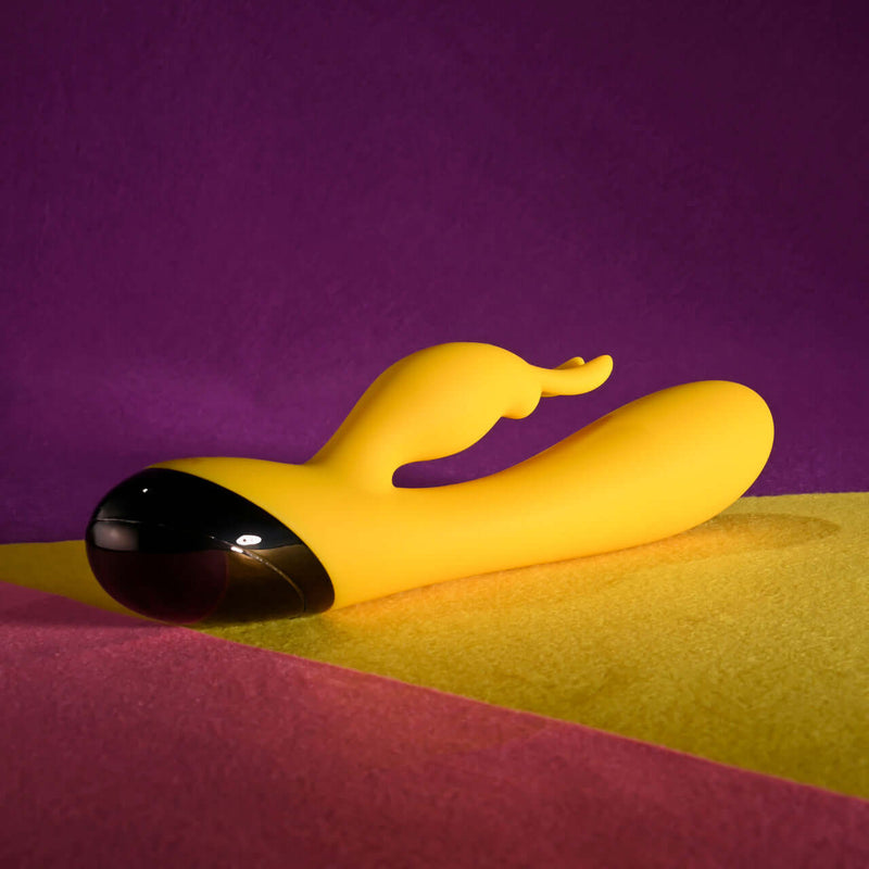 Selopa Buzzz Bunny Rechargeable Silicone Rabbit Vibrator in yellow with black accents on colorful background.
