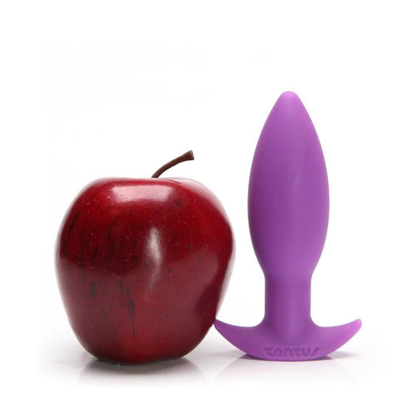 Neo Purple Anal Plug by Tantus beside a shiny red apple for size comparison, highlighting its beginner-friendly tapered design.
