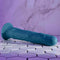 Evolved Tsunami realistic vibrator with undulating waves and remote control on tile floor against a purple marble background