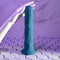 Realistic blue vibrator with crowned head and textured shaft on white hex tile, hand touching it