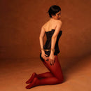 A model wearing a black corset and red tights poses on her knees, showcasing an artistic and stylish look.
