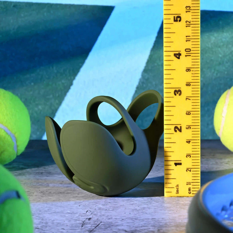 Zero Tolerance Nutty Buddy Dual Cock Ring in green, showing size comparison with measuring tape, surrounded by tennis balls.