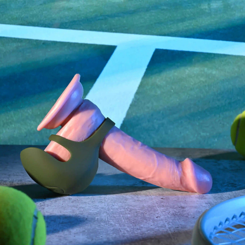 Zero Tolerance Nutty Buddy green silicone dual cock ring with textured shield on a tennis court.