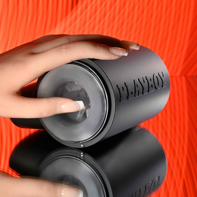 Playboy Come Along travel-sized stroker with dual entry, held by a hand against an orange background