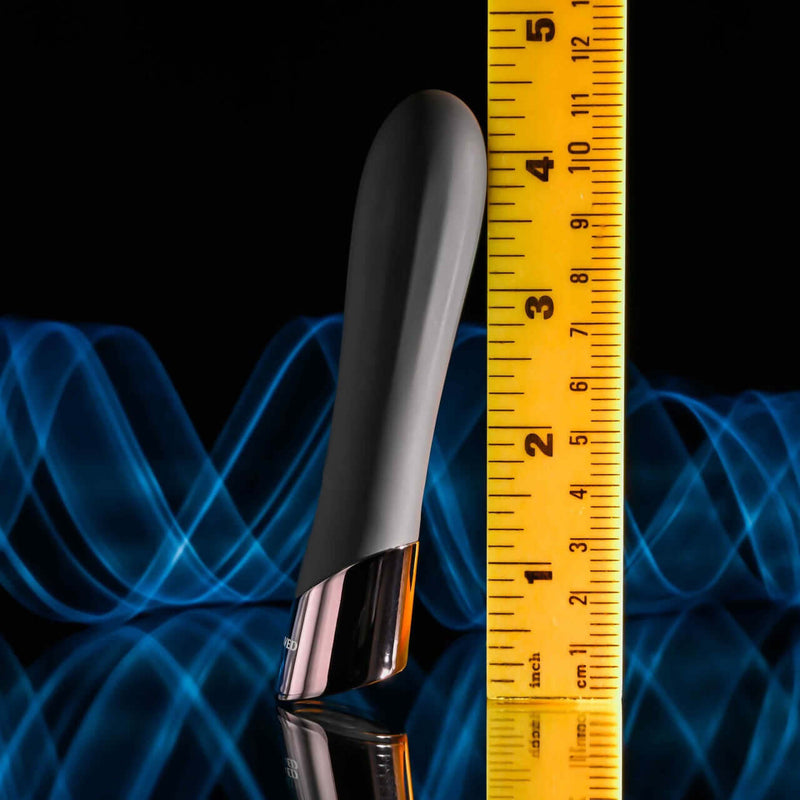 Evolved Back in Black Petite Vibrator beside a yellow ruler against a blue wavy background, showcasing size and sleek design.