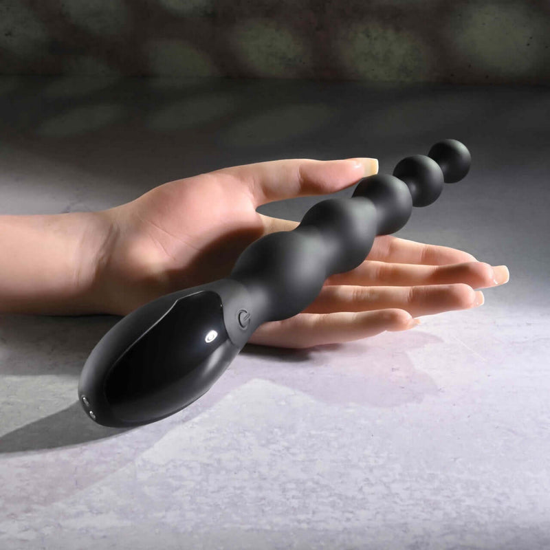 Flexible beaded vibrator with 9 speeds for intense backdoor play held in hand on a concrete surface