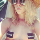 Woman wearing Pastease Black Censor Bars Pasties with sunglasses and a straw hat, showcasing playful confidence.