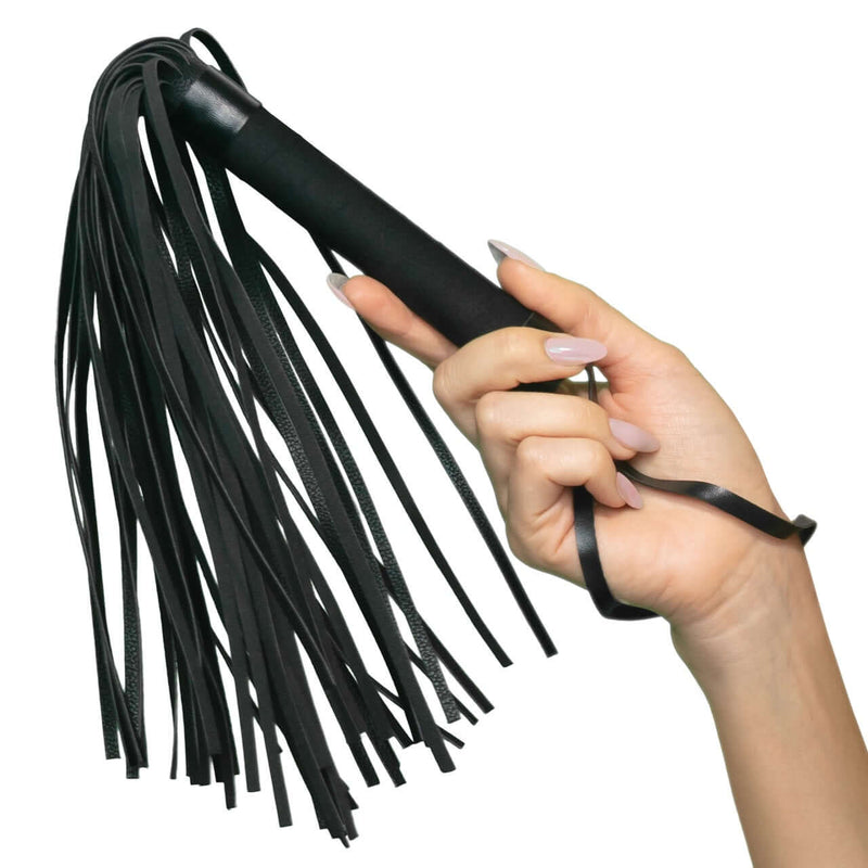 Hand holding Nocturnal™ Collection Flogger with black leather strands and sturdy handle for sensory play. Ideal for newcomers and enthusiasts.