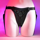 Fully adjustable faux-leather strap-on harness from Gender X, showcasing secure waist and leg straps on a mannequin with a pink background