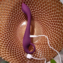Evolved Lochness G Vibrator with arched shaft and ring handle, shown charging with USB cable on a textured golden surface
