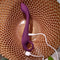 Evolved Lochness G Vibrator with arched shaft and ring handle, shown charging with USB cable on a textured golden surface