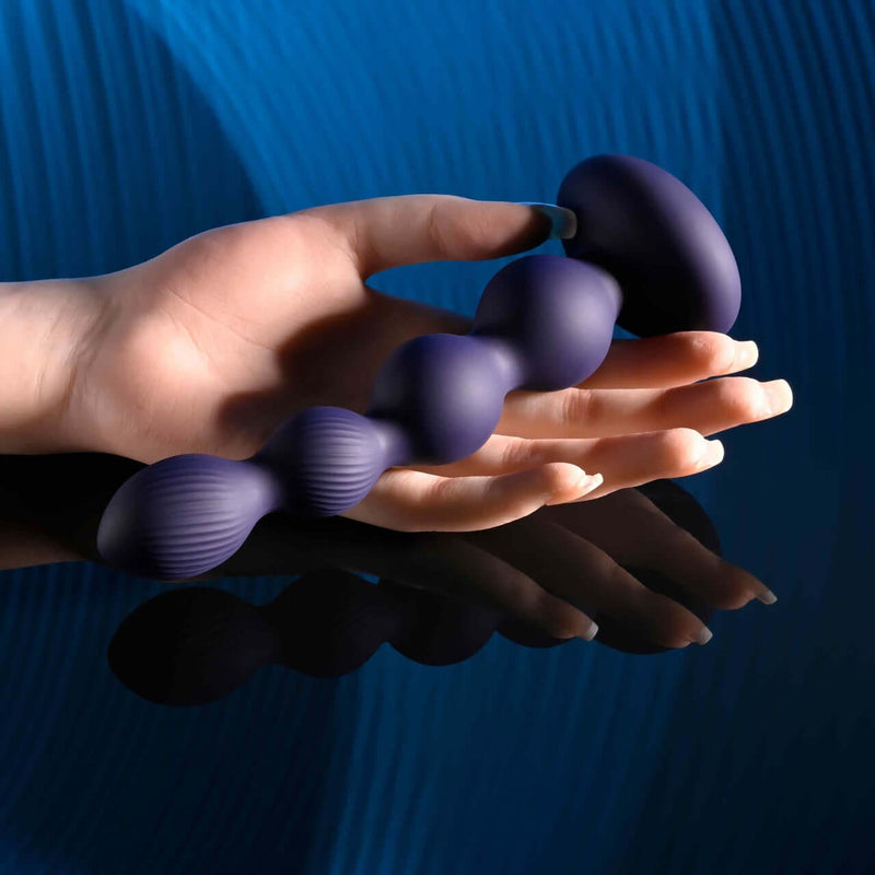 Hand holding Evolved Pleasure Orbit Remote Control Twirling & Vibrating Bulbed Shaft on blue background