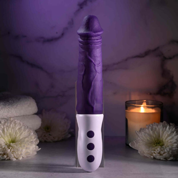 EVOLVED Plum Thrust powerful thrusting vibrator with realistic design and USB rechargeable, set against a serene candle-lit background.