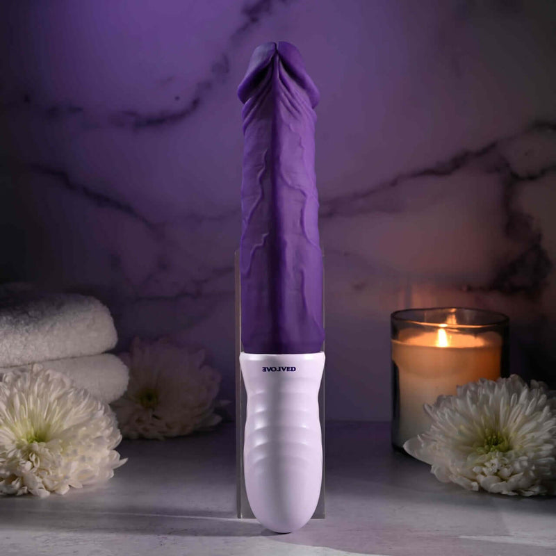 The EVOLVED Plum Thrust powerful thrusting vibrator with realistic design and USB rechargeable feature displayed with candles and flowers.